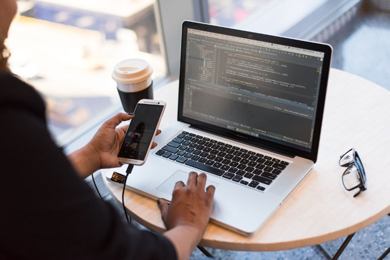 Web development on a laptop while holding a smartphone
