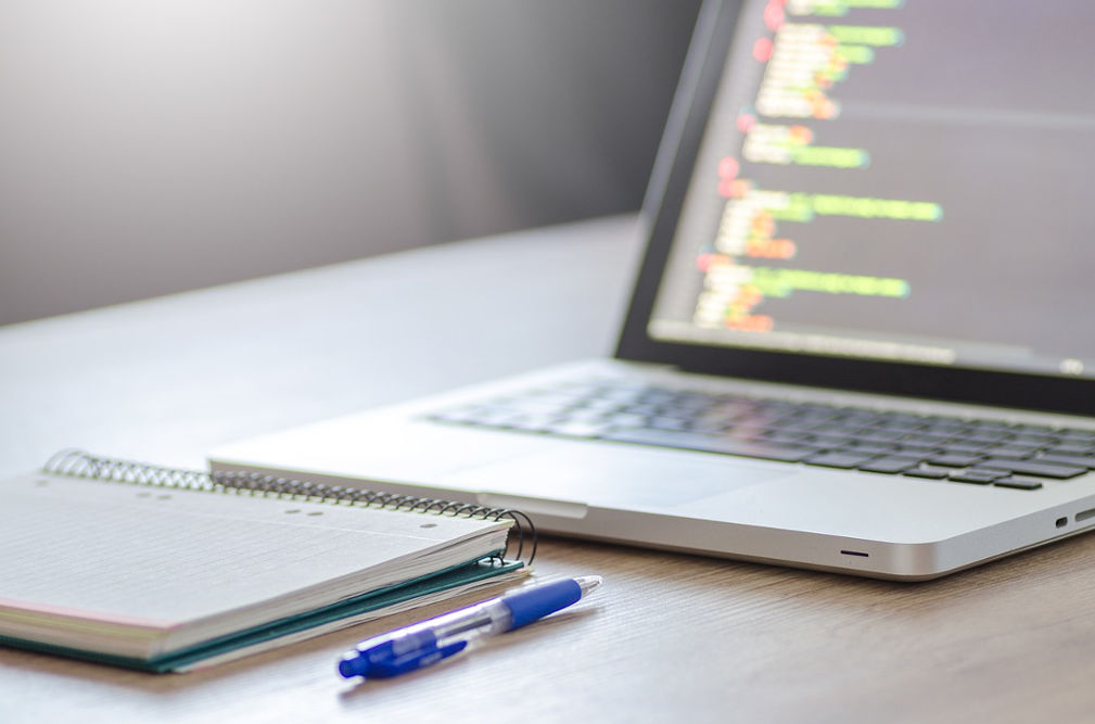 A Macbook, a notebook, and a pen